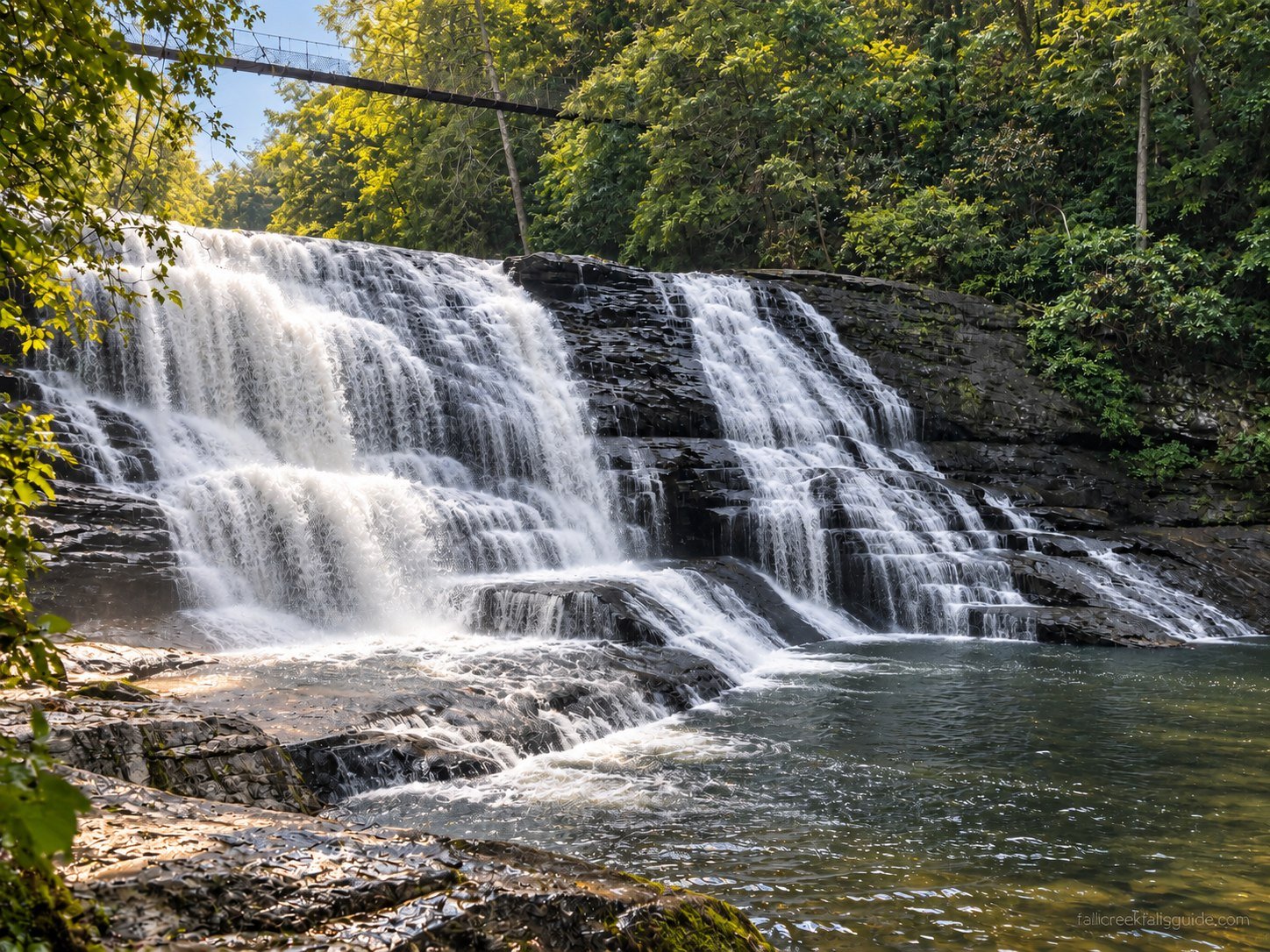 Cane Creek Cascades flowing over broad layered rock beneath the suspension bridge at Fall Creek Falls State Park